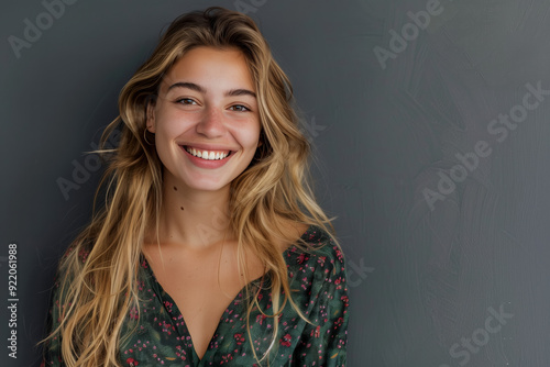 Portrait of a smiling blonde girl in a casual style against a gray background.