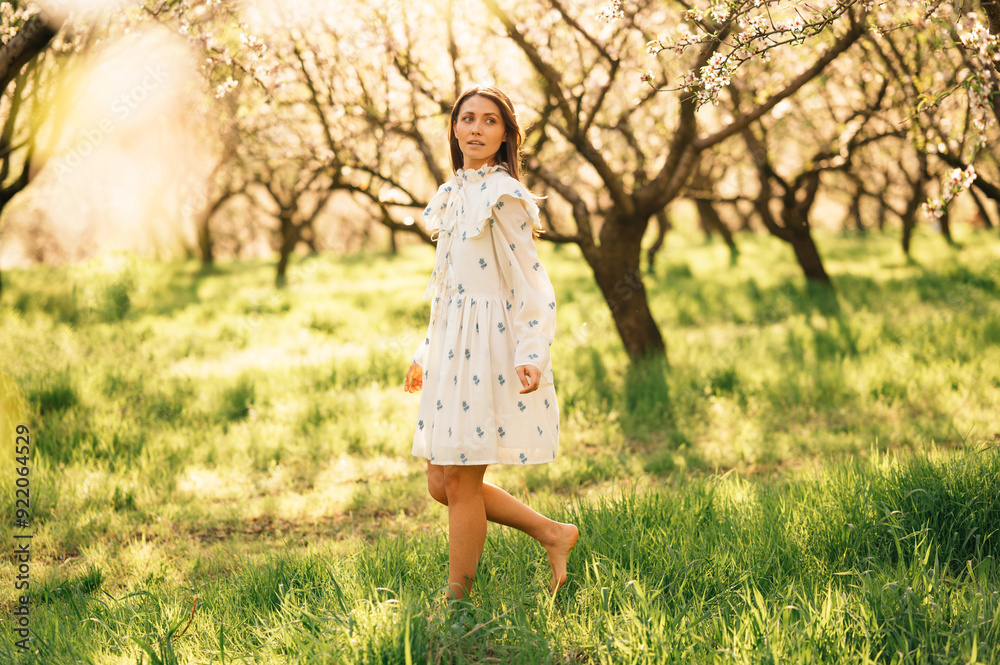 An elegantly dressed woman in a beautiful floral dress is enjoying a sunny day inside a blooming orchard