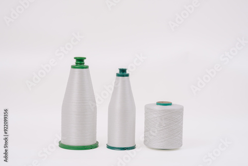 Three spools of white fiberglass yarn, two cone-shaped and one cylindrical, arranged on a plain background, showcasing different textures and shapes. photo