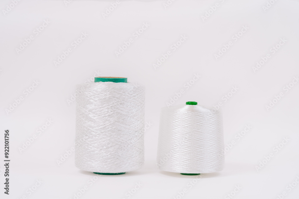 Obraz premium Two spools of white fiberglass thread with green cores, placed side by side on a white background, showcasing different sizes.