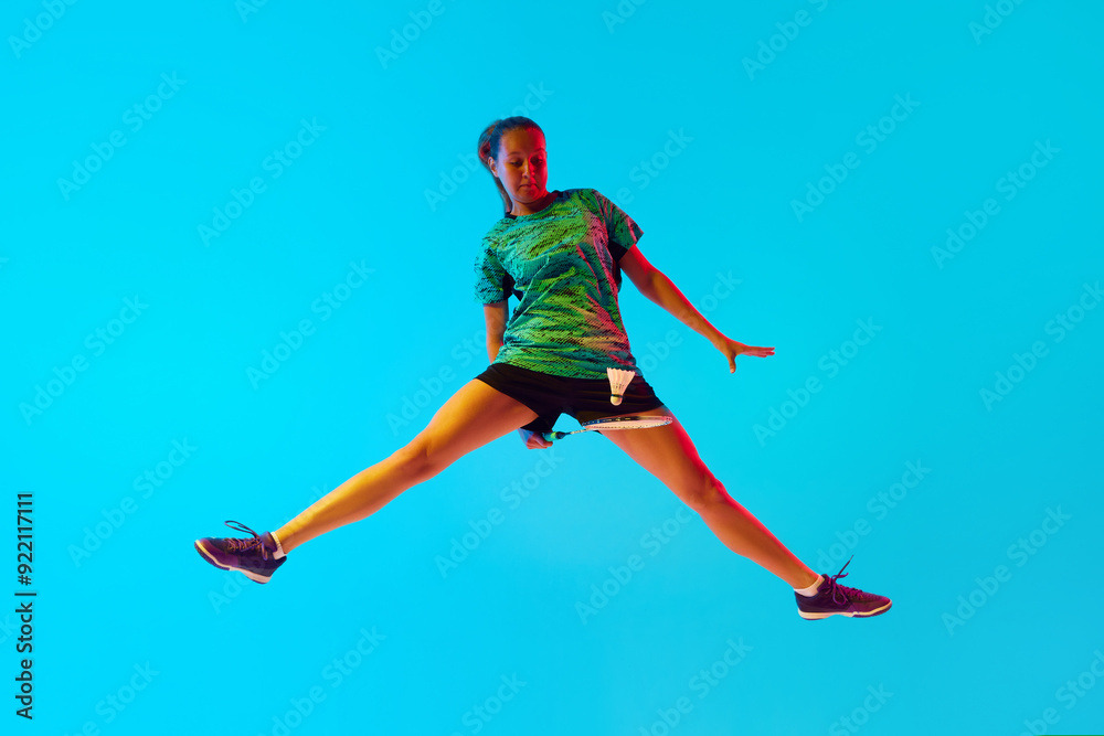 Obraz premium Impressive movement of female badminton player hitting shuttlecock in neon light against gradient blue background. Concept of individual sport, tournament, match, championship. Ad