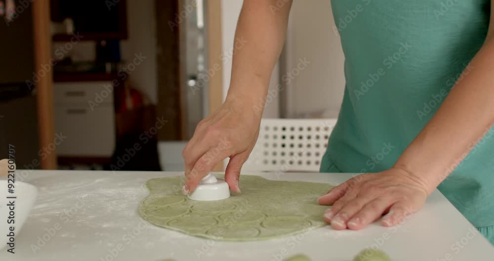 A closeup shot capturing hand meticulously shaping vibrant green dough on a kitchen counter, preparing it for baking She makes round molds for the dough. A closeup shot capturing hand meticulously shaping vibrant green dough on a kitchen counter, preparing it for baking She makes round molds for the dough.