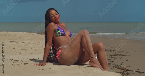 A tropical beach scene with a young girl sitting in the sand in a bikini soaking up the sun photo