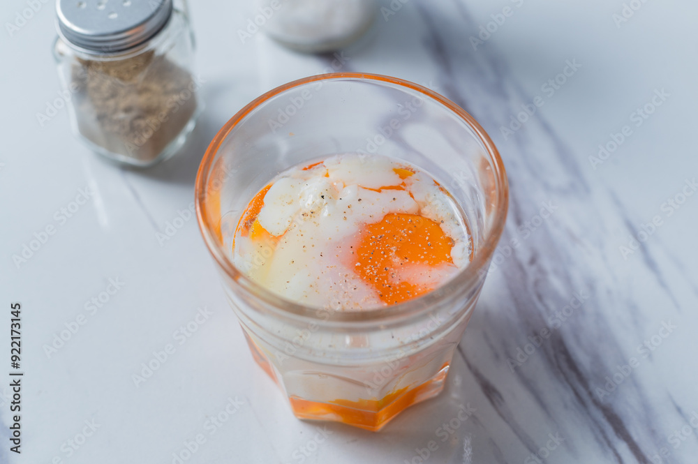 A glass of soft-boiled egg seasoned with salt and pepper, with a touch of soy sauce, placed on a marble surface, ideal for breakfast content or culinary presentations focused on nutritious meals. A glass of soft-boiled egg seasoned with salt and pepper, with a touch of soy sauce, placed on a marble surface, ideal for breakfast content or culinary presentations focused on nutritious meals.