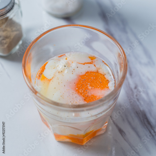 A glass of soft-boiled egg seasoned with salt and pepper, with a touch of soy sauce, placed on a marble surface, ideal for breakfast content or culinary presentations focused on nutritious meals. photo