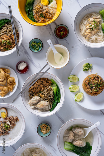 An overhead shot of a variety of Asian dishes including noodles, rice, soup, and wontons, arranged on a marble table, ideal for showcasing a diverse culinary spread perfect for food photography