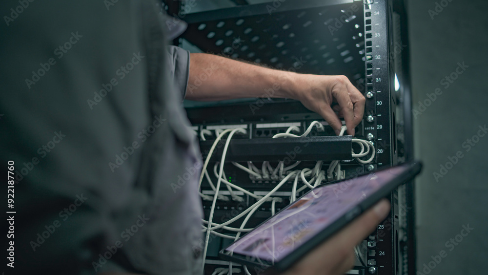 Naklejka premium Male specialist inserts cable into server rack. Network administrator works in server room using tablet computer. Maintenance of computer networks or web servers. Data storage center. Slow motion.
