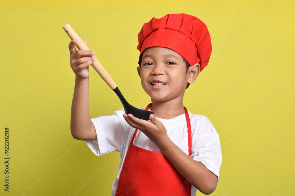 Cute little chef holding ladle isolated on yellow background. Asian boy cooking Cute little chef holding ladle isolated on yellow background. Asian boy cooking