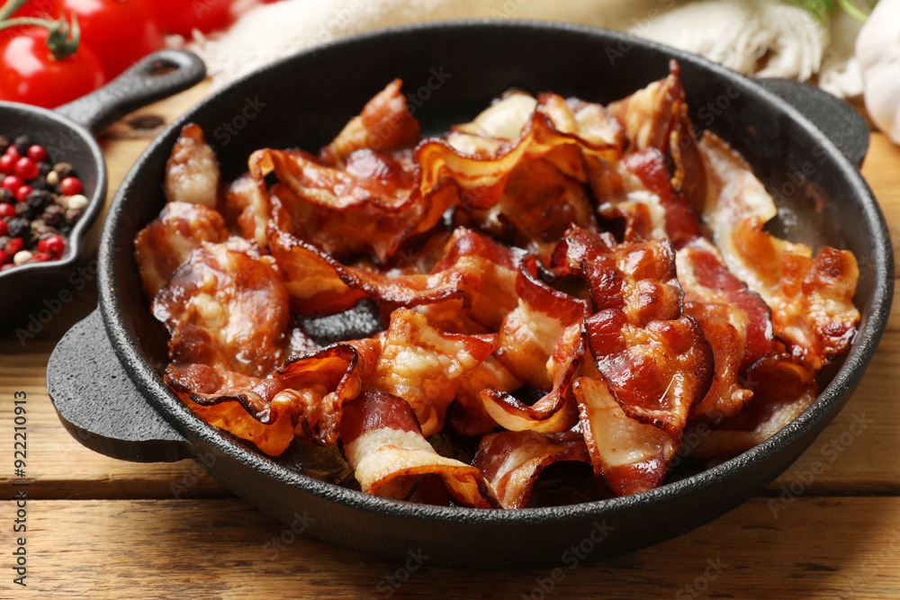 Delicious bacon slices in frying pan and products on wooden table, closeup Delicious bacon slices in frying pan and products on wooden table, closeup