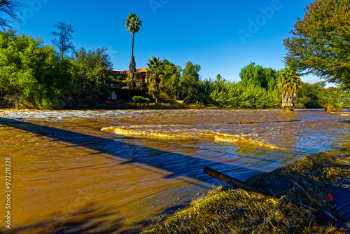 Flooded river that's burst it's banks with destroyed fence following heavy rains in Oudtshoorn, Western Cape, South Africa photo