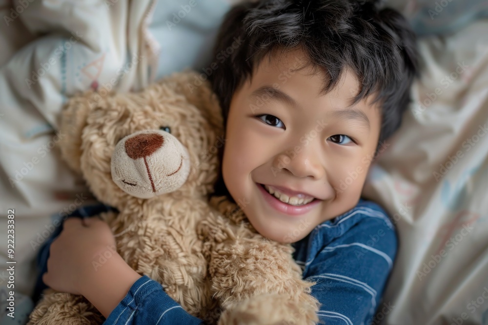 A young boy in a striped shirt hugs a teddy bear while lying in bed, smiling warmly at the camera, presenting a comforting and happy childhood moment. A young boy in a striped shirt hugs a teddy bear while lying in bed, smiling warmly at the camera, presenting a comforting and happy childhood moment.