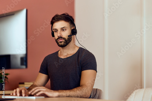 A busy man is working online, over the laptop, at the office, wearing headphones.