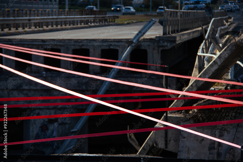 A detailed close-up of tensioned red straps securely fastened with a metal hook on a gravel surface, demonstrating precision and strength in securing elements.