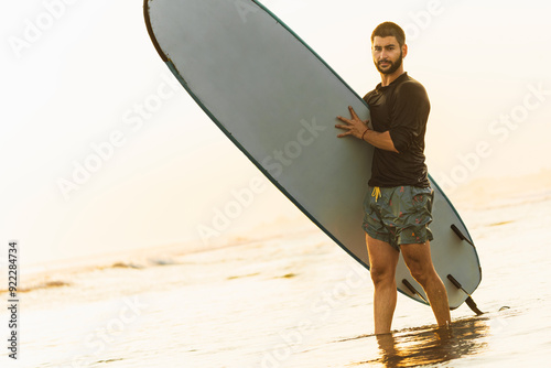 Canvas Print Attractive man holding his surfboard on the shore of the beach