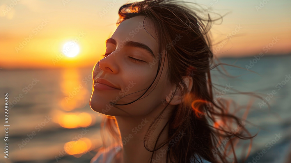 Charming woman with closed eyes near the sea, basking in the last rays of the sun, expressing delight at sunset Charming woman with closed eyes near the sea, basking in the last rays of the sun, expressing delight at sunset