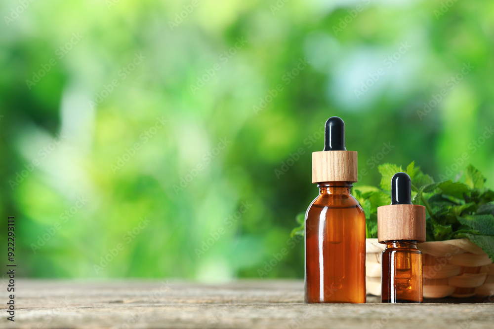 Bottles of mint essential oil and fresh leaves on wooden table, space for text