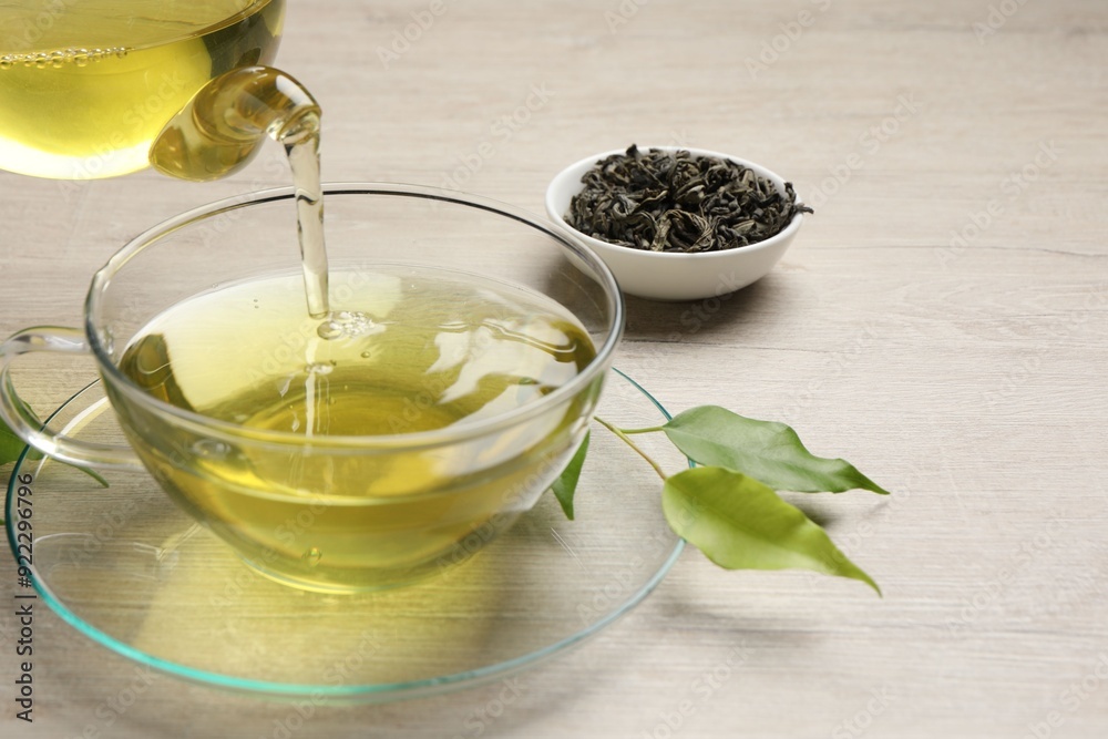 Pouring refreshing green tea into cup at wooden table, closeup Pouring refreshing green tea into cup at wooden table, closeup