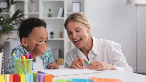 Adorable little african american boy with curly hair having fun at pediatric specialist appointment, happy child drawing with female therapist, exercises for children with autism.