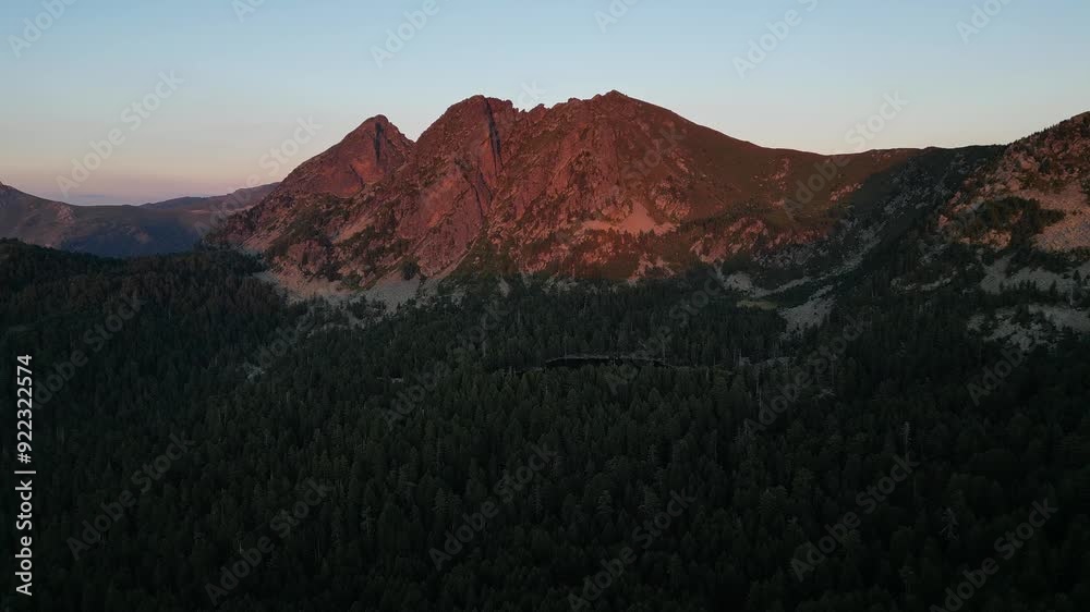 Aerial view of a picturesque mountain peak illuminated by the setting sun and surrounded by dense forest