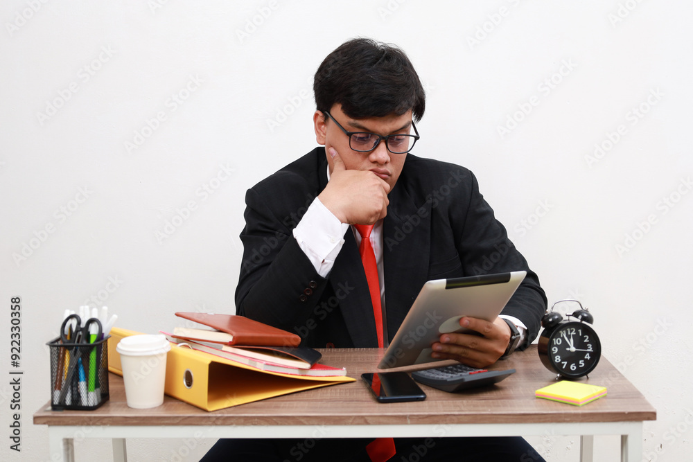 Unhappy male working in the office sitting on office desk while using tablet computer, front view, isolated on white. Unhappy male working in the office sitting on office desk while using tablet computer, front view, isolated on white.