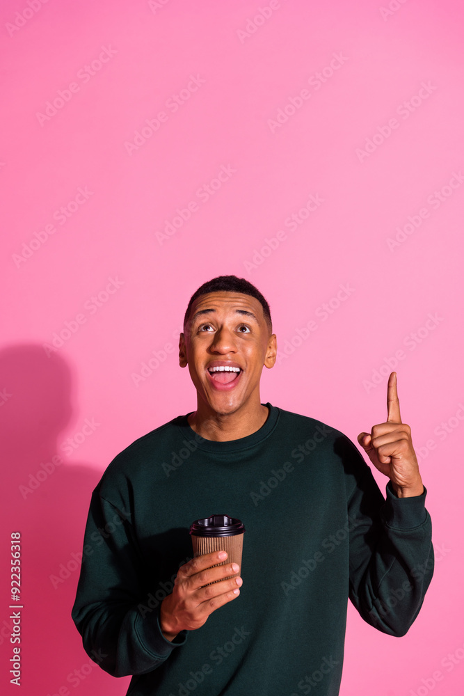 Vertical photo of attractive funny guy wear sweatshirt drink beverage pointing up emtpy space isolated pink color background