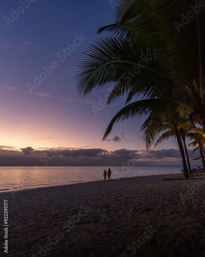 A couple walks at Flic en Flac beach at sunset in Mauritius, Africa.