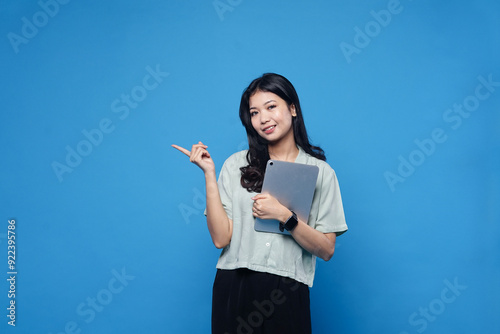 Excited korean woman with digital tablet, pointing at empty space, advertisement banner, holding gadget, showing promo offer, blue background.