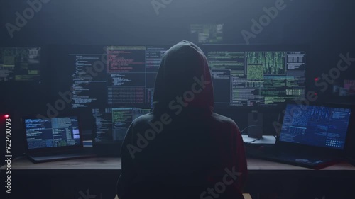 A shadowy outline of a hacker dressed in a hoodie, deeply focused on multiple screens displaying code and data