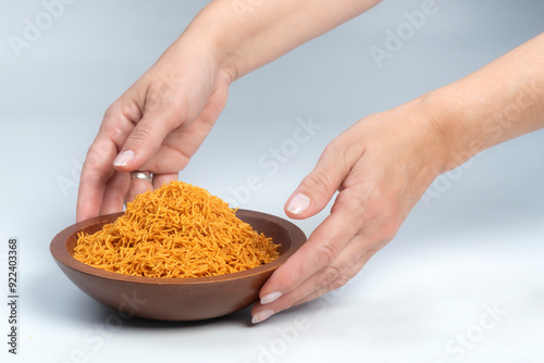 Studio shot of female hands holding a carved wooden bowl containing a heap of tikha sev, isolated on white photo