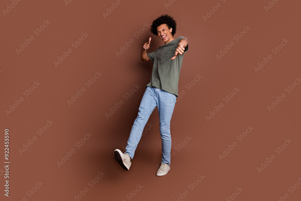 Photo of youngster guy with wavy hair in gray t shirt and jeans casual outfit pointing fingers invites you party isolated on brown color background Photo of youngster guy with wavy hair in gray t shirt and jeans casual outfit pointing fingers invites you party isolated on brown color background
