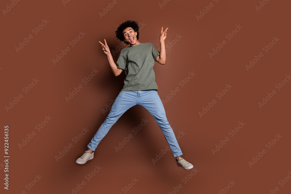 Full size photo of nice young guy jump show v-sign wear trendy khaki outfit isolated on brown color background Full size photo of nice young guy jump show v-sign wear trendy khaki outfit isolated on brown color background