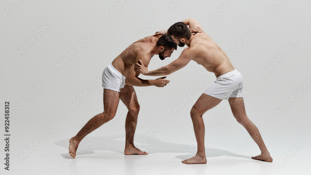 Two athletes engage in gripping wrestling match, their muscular forms locked in fierce contest of strength against warm grey background. Concept of health, beauty and fashion, fitness, masculinity. Two athletes engage in gripping wrestling match, their muscular forms locked in fierce contest of strength against warm grey background. Concept of health, beauty and fashion, fitness, masculinity.