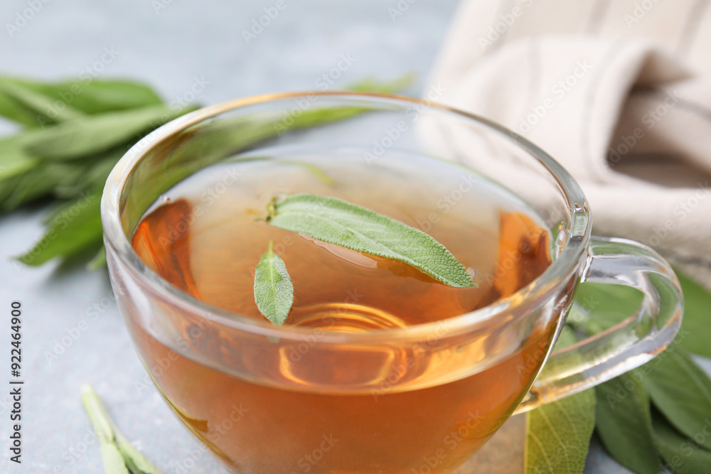 Aromatic herbal tea in cup with sage on grey table, closeup Aromatic herbal tea in cup with sage on grey table, closeup