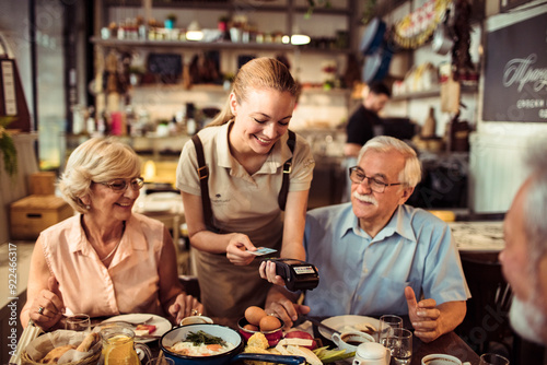 Senior man paying with smartphone for meal with friends at a restaurant