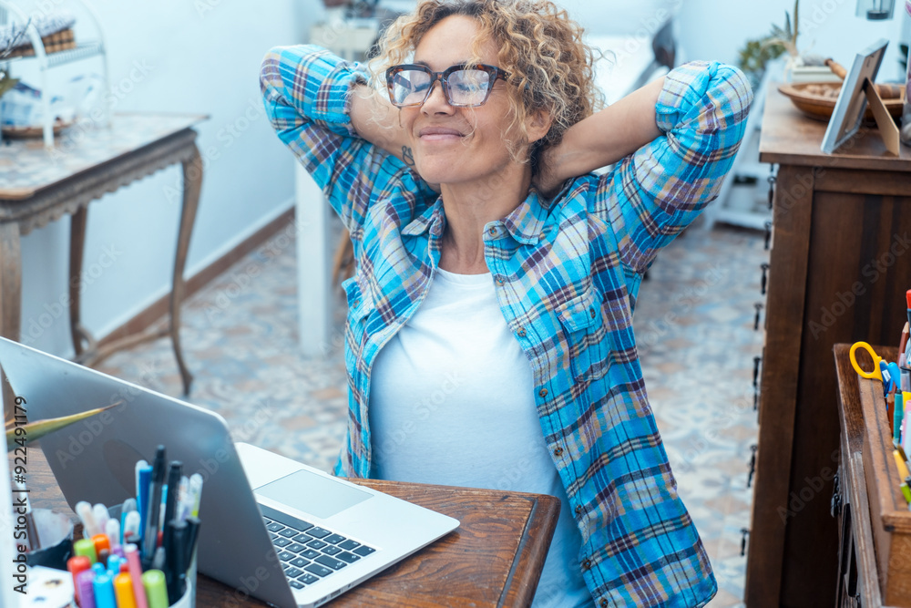 © simona - Adult woman sitting at her home office desk, stretching her back and shoulders with a happy, satisfied expression after completing work, embodying the freelance lifestyle of remote online work © simona - Adult woman sitting at her home office desk, stretching her back and shoulders with a happy, satisfied expression after completing work, embodying the freelance lifestyle of remote online work