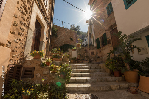 Fototapeta Naklejka Na Ścianę i Meble -  a small street over some steps in a small town in Mallorca, Spain, with rays of sun shining onto the building on the side