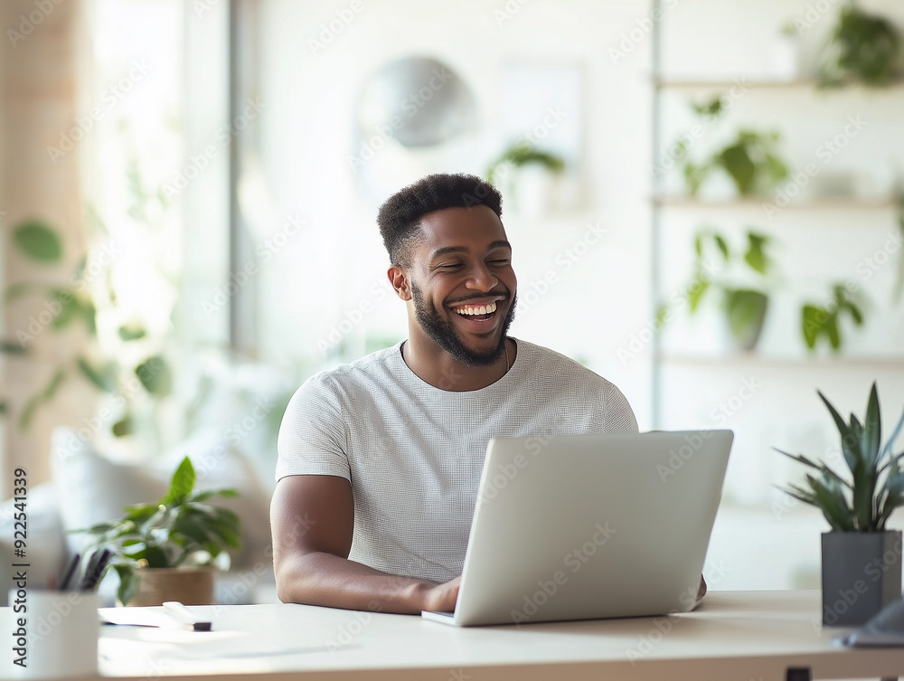 A smiling man working on his laptop in a bright and modern home office environment, reflecting productivity and a positive work-life balance. A smiling man working on his laptop in a bright and modern home office environment, reflecting productivity and a positive work-life balance.