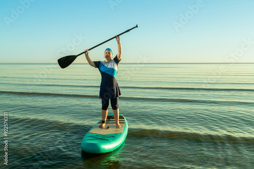 Fotografia A woman in a modest burkini on a paddle board with a raised paddle in the sea ag