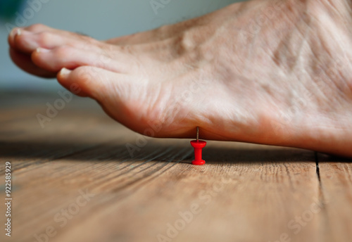 A person's barefoot stepping on a red pushpin tack photo