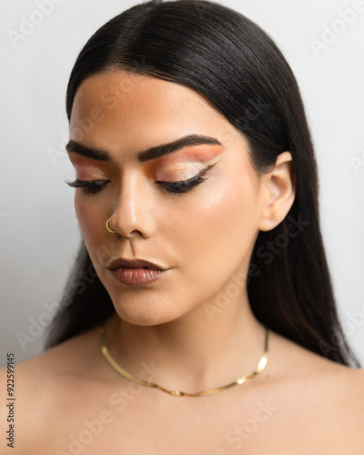 Beauty eye makeup on Brazilian model with subtle and artistic makeup look featuring soft peach and gold eyeshadow, precise black eyeliner with a winged tip, and glossy brown lipstick