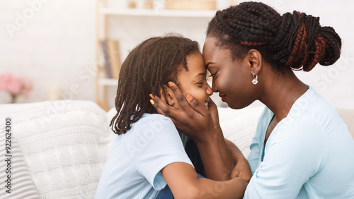 Love Of Black Mom And Daughter. Happy afro woman cuddling her dear child on couch at home