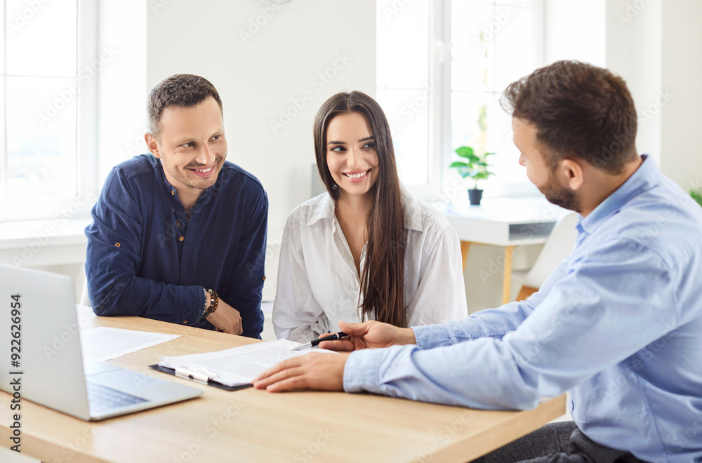 Young couple sitting with male business broker or insurance agent showing documents sitting at the desk with laptop in office. Clients having consultation with man realtor or financial advisor. Young couple sitting with male business broker or insurance agent showing documents sitting at the desk with laptop in office. Clients having consultation with man realtor or financial advisor.