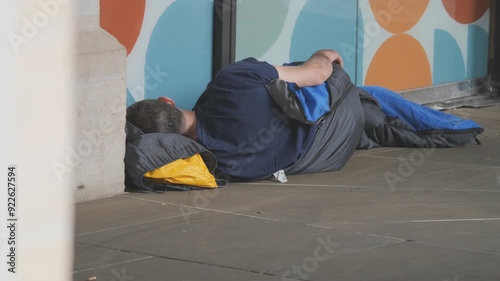 A homeless man sleeping on a street in a sleeping bag.