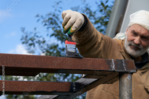 A grown man paints a metal structure with anti-corrosion paint. photo