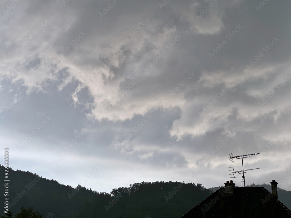 Overcast Sky with Thick Rain Clouds Hovering Above Forested Hills and a Rooftop with TV Antennas, Signifying an Imminent Downpour Overcast Sky with Thick Rain Clouds Hovering Above Forested Hills and a Rooftop with TV Antennas, Signifying an Imminent Downpour