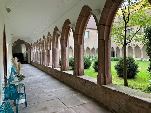 Cloister Corridor of the Couvent des Dominicains de Guebwiller Overlooking a Lush Courtyard Garden with Gothic Arches and Stone Walkway, Florival, Haut-Rhin, Alsace, France photo