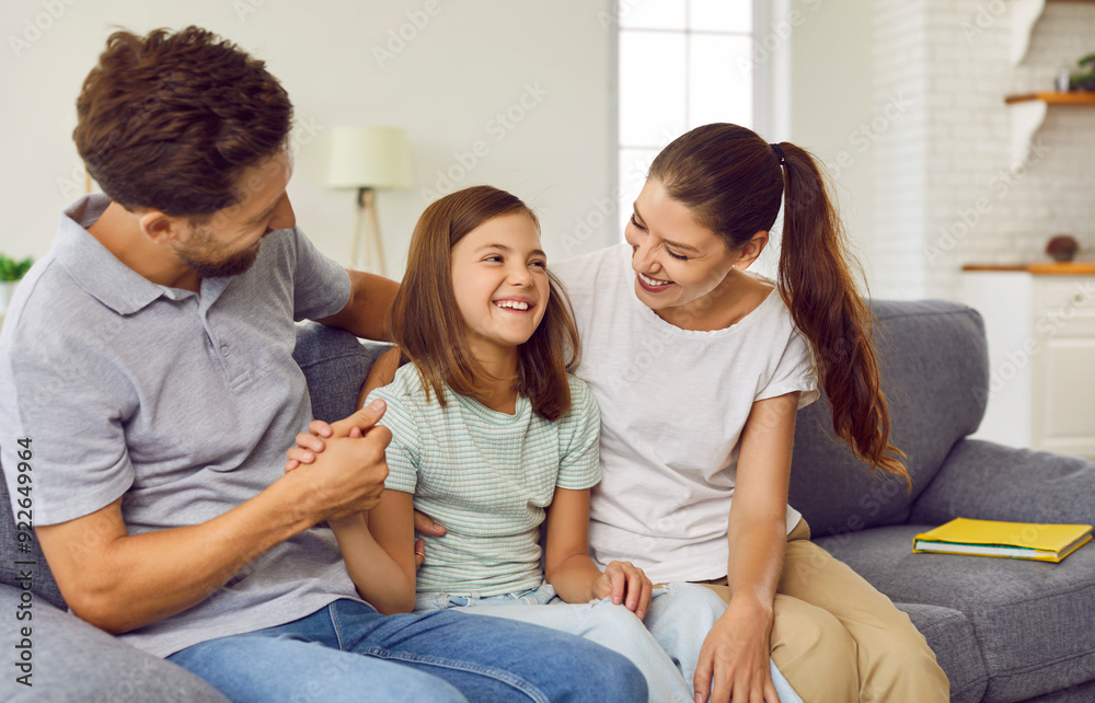 Happy nuclear family having fun at home. Cheerful mother, father and child daughter sitting on the sofa in the living room and laughing at a funny joke together Happy nuclear family having fun at home. Cheerful mother, father and child daughter sitting on the sofa in the living room and laughing at a funny joke together