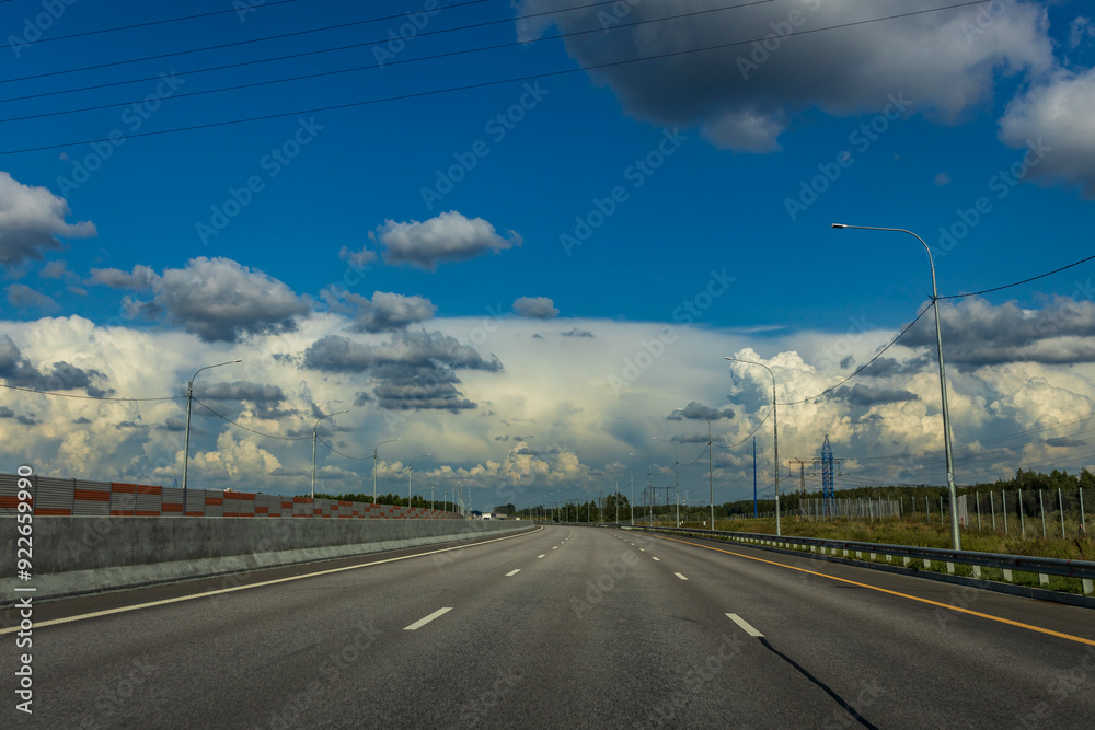 Fototapeta premium A long, empty highway with a few trees in the background