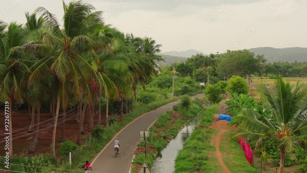 An old man cycling through the countryside on a road beside a water canal An old man cycling through the countryside on a road beside a water canal