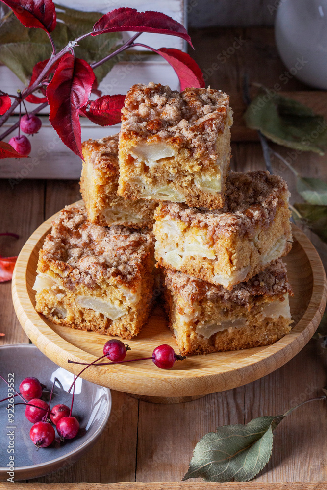 Slices of Dutch apple cake with streusel on a wooden tray, apples and apple branches on a wooden background.